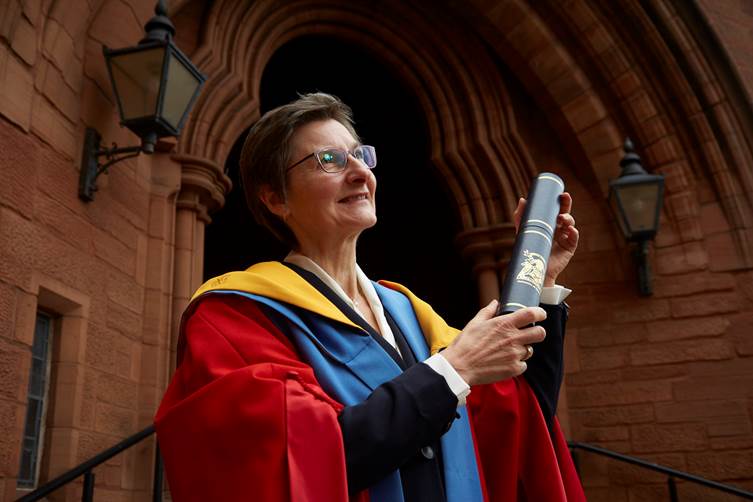 A person in a robe holding a diploma

Description automatically generated